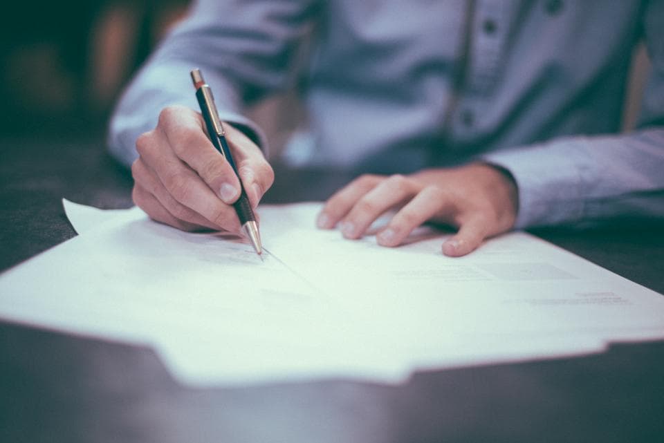 Hands writing notes on a pad beside a laptop