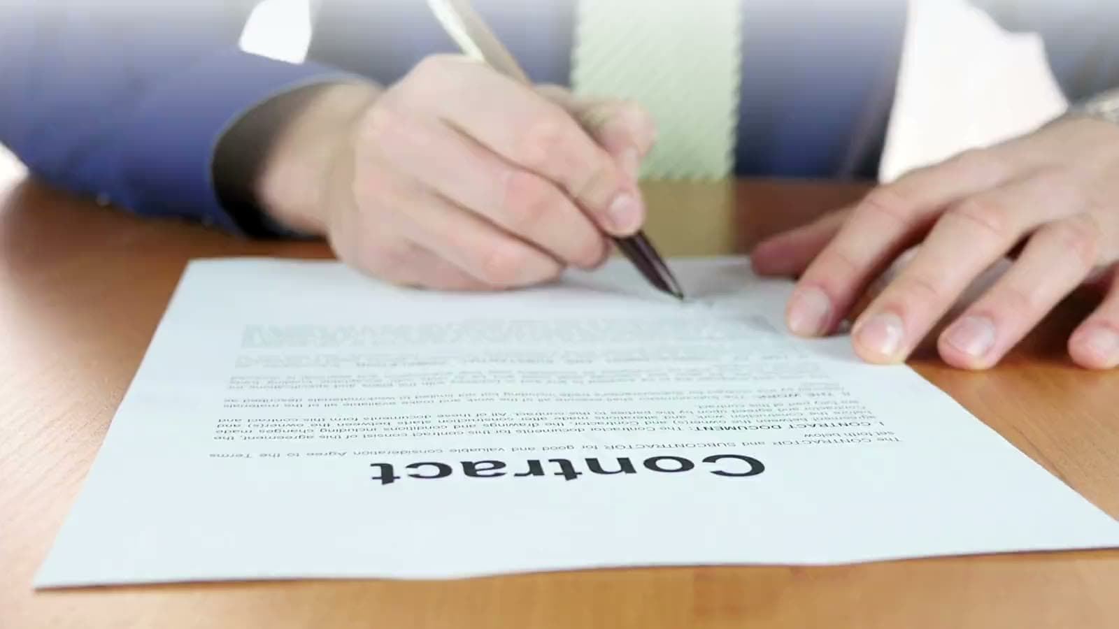 A client signing a contract at a wooden desk with a fountain pen